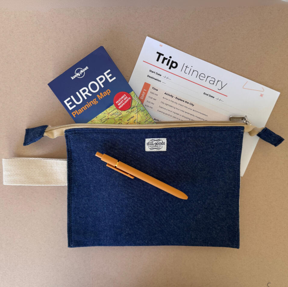Accordion Travel Organizer Navy cotton zip pouch with the StillGoods Studio label, holding a travel itinerary and Europe guidebook, with a pen tucked into its canvas strap.